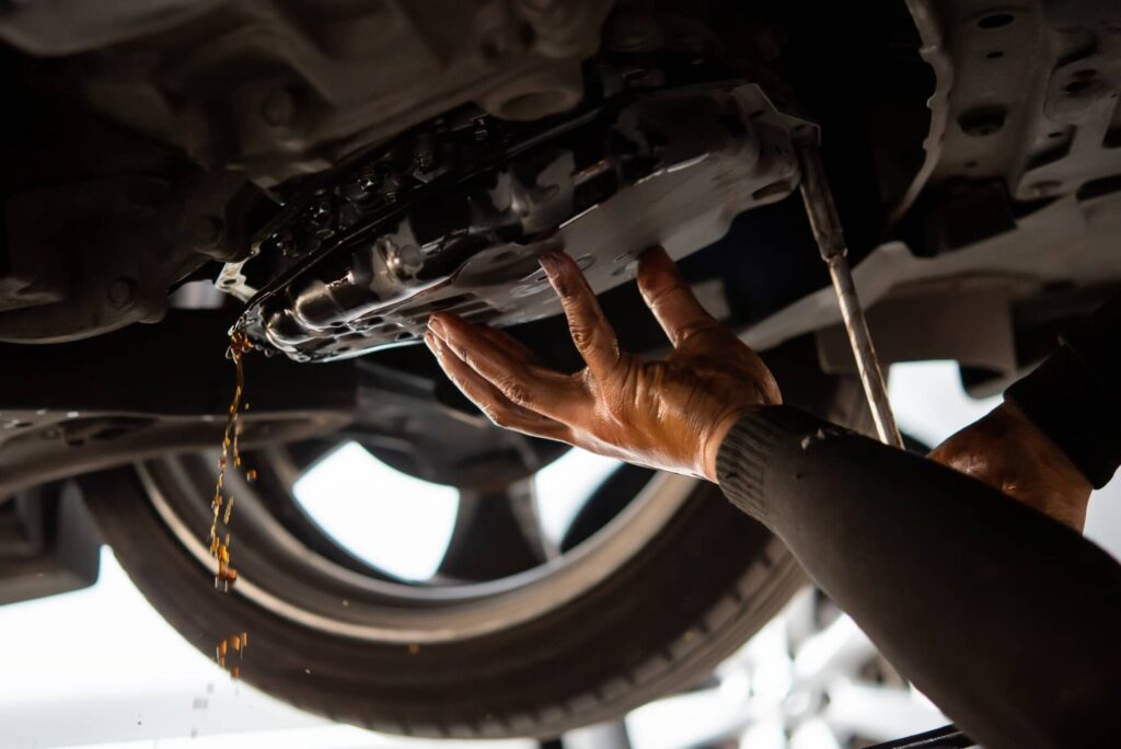 Car mechanic underneath a vehicle draining the old automatic transmission fluid.